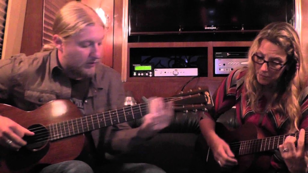Derek Trucks and Susan Tedeschi playing acoustic guitars on a tour bus.