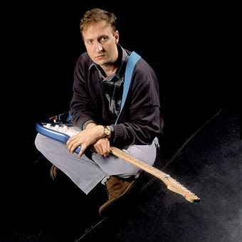 Bob Mould seated with electric guitar across lap