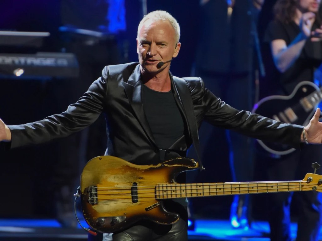 Sting with arms outstretched at microphone with bass guitar