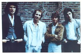 Group shot of the band Dire Straits outdoors in front of brick wall