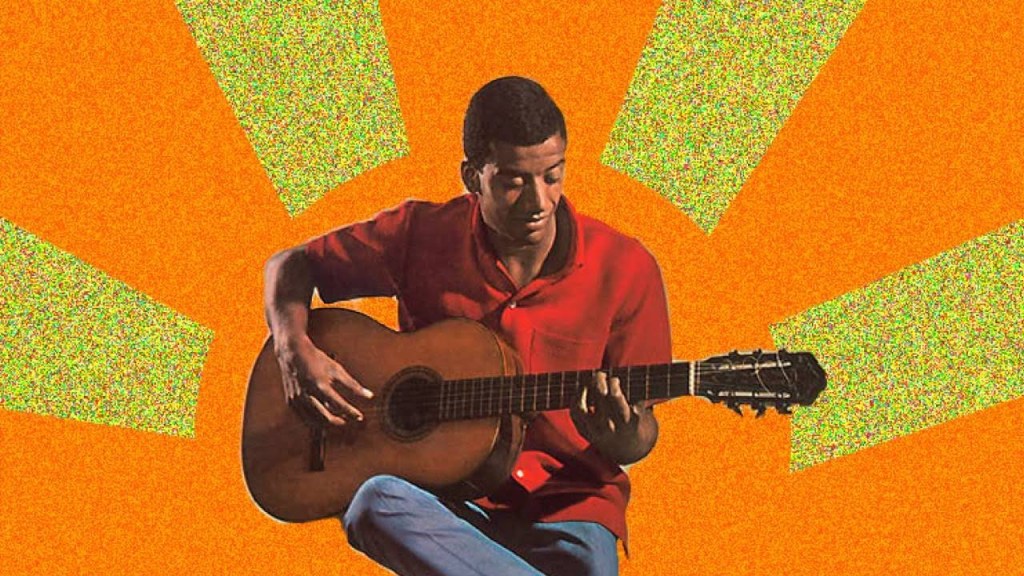 Singer - guitarist Jorge Ben seated with acoustic guitar in front of brightly colored display.