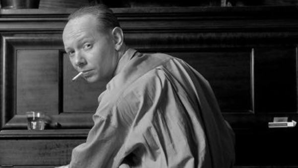 Singer Joe Jackson sitting at piano - photo taken from behind with him looking over his shoulder at the camera