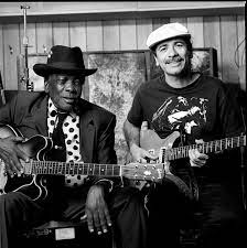 A seated John Lee Hooker (left) and Carlos Santana (right) both holding electric guitars.