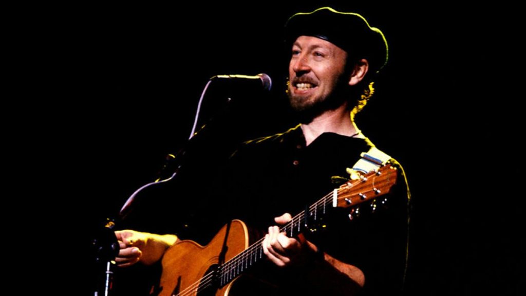 Singer and guitarist Richard Thompson on stage holding acoustic guitar wearing a beret
