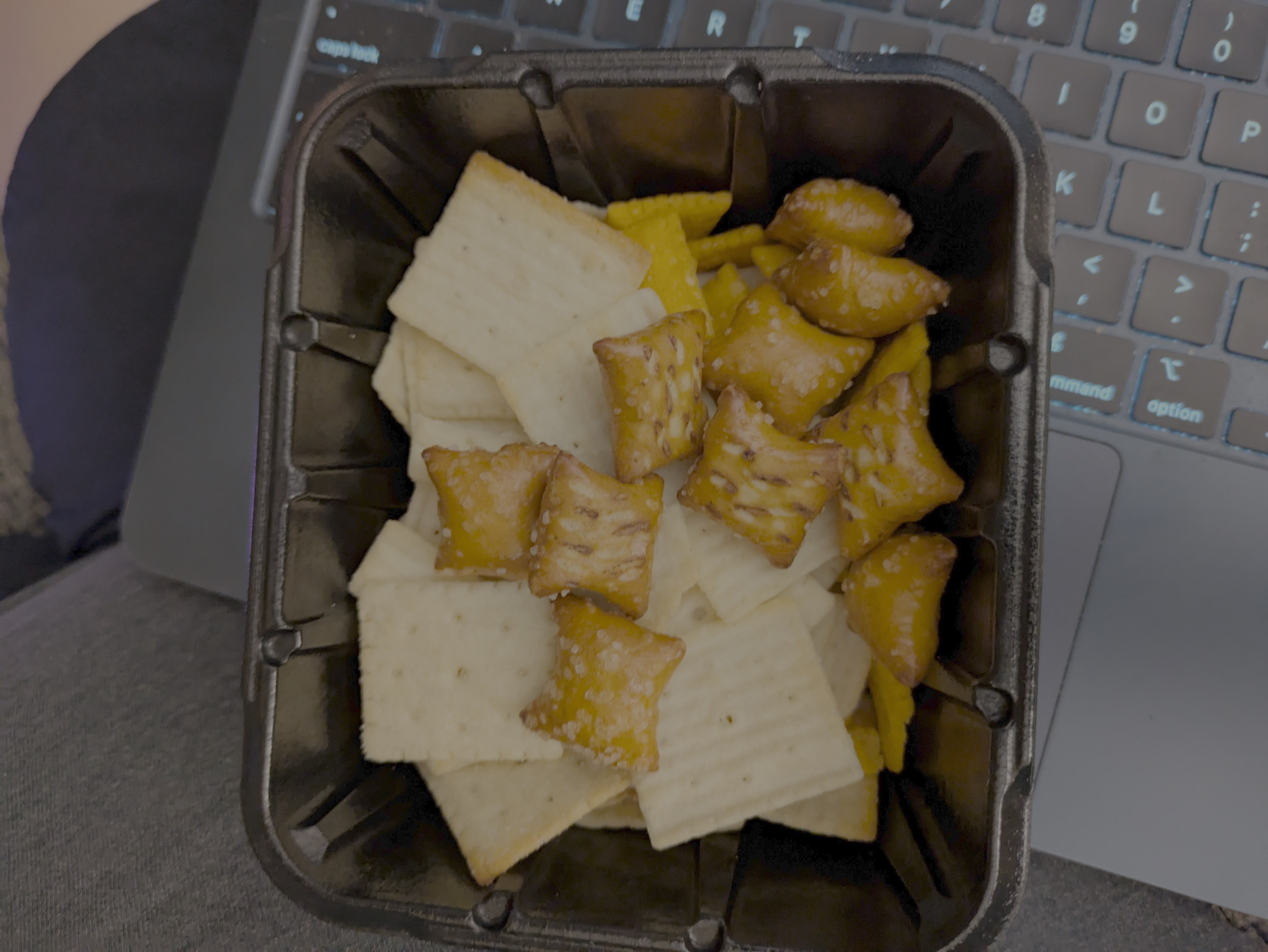 A small black plastic container filled with crackers and pretzels.
