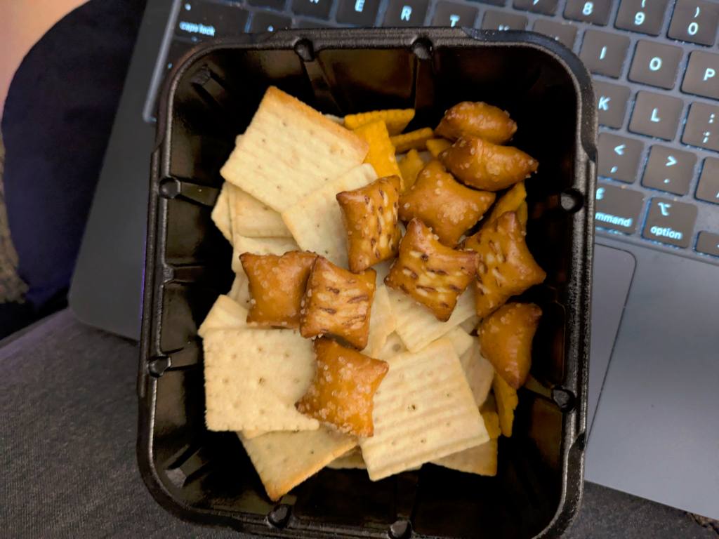 A small black plastic container filled with crackers and pretzels.