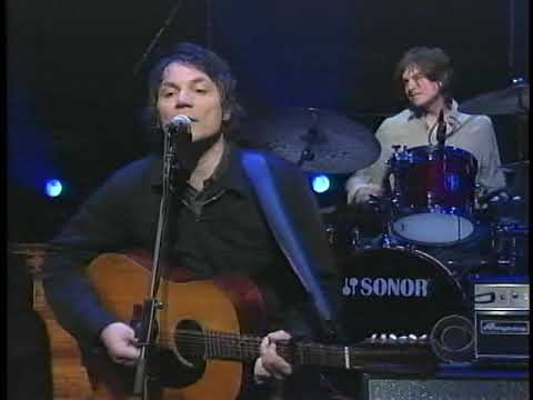 Jeff Tweedy of Wilco performing on stage in front of drummer in background