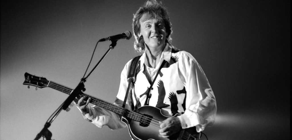 Paul McCartney on stage in front of microphone with signature Hofner bass.