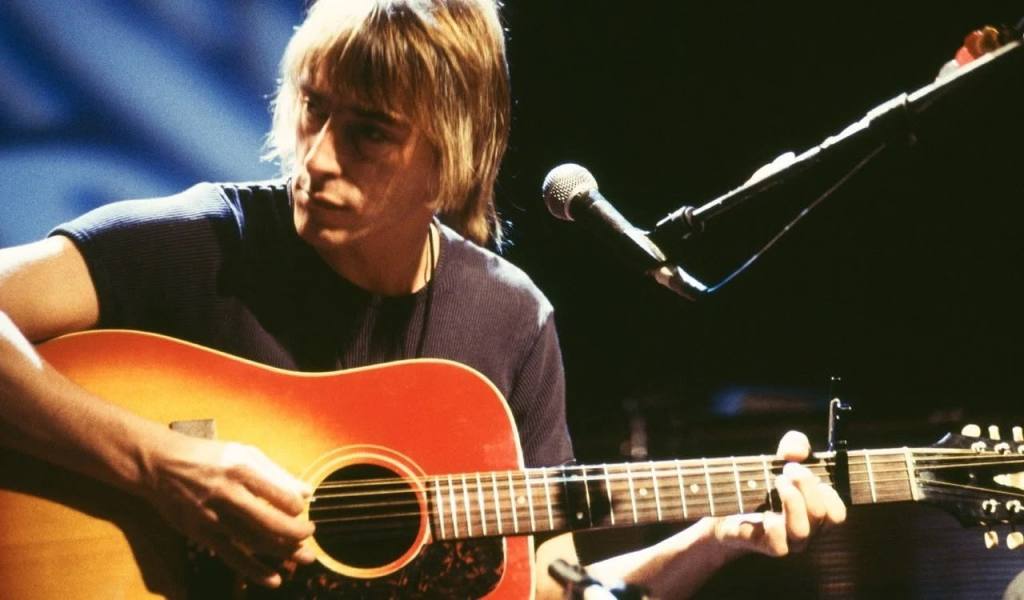 Singer Paul Wellet seated on stage in front of microphone holding acoustic guitar