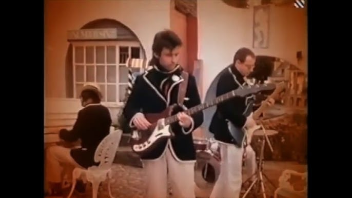 The band XTC in matching outfits for a music video shoot playing outdoors.