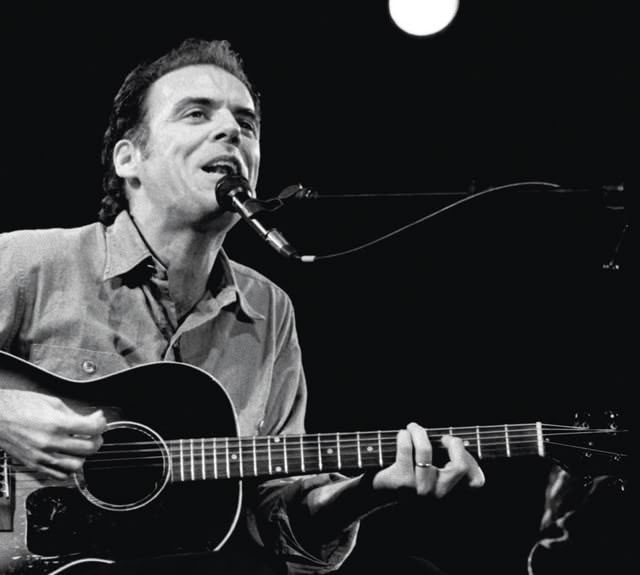 Singer / Songwriter John Hiatt playing an acoustic guitar, singing in to microphone.