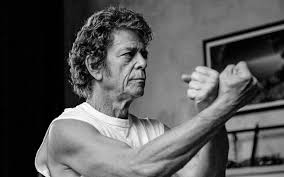 Lou Reed in a sleeveless white tee in a fists up boxing pose.