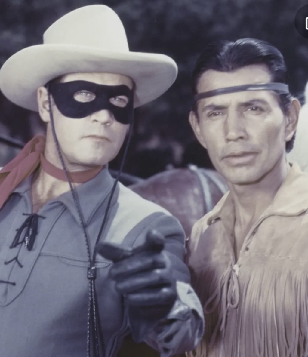 The Lone Ranger and Tonto outdoors in full character dress, the lone ranger pointing to something unseen off screen.